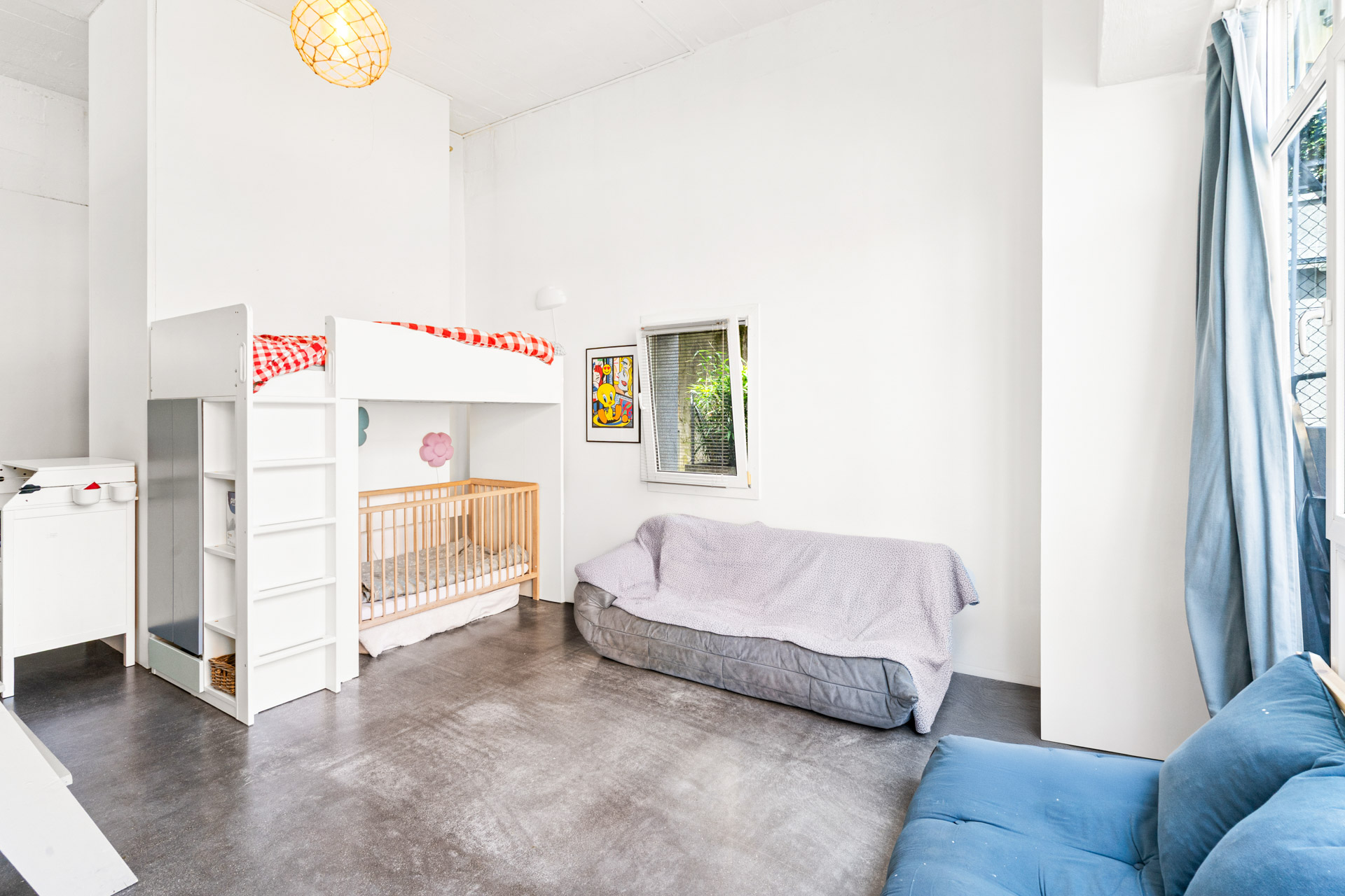 Chambre lumineuse avec lit mezzanine, espace canapé et grande hauteur sous plafond