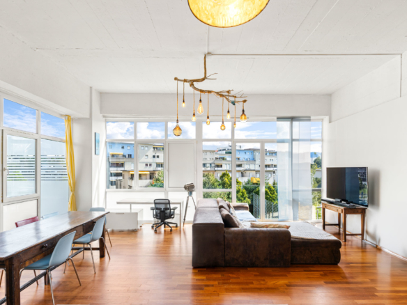 Salon spacieux et lumineux avec parquet, canapé d’angle et grandes baies vitrées