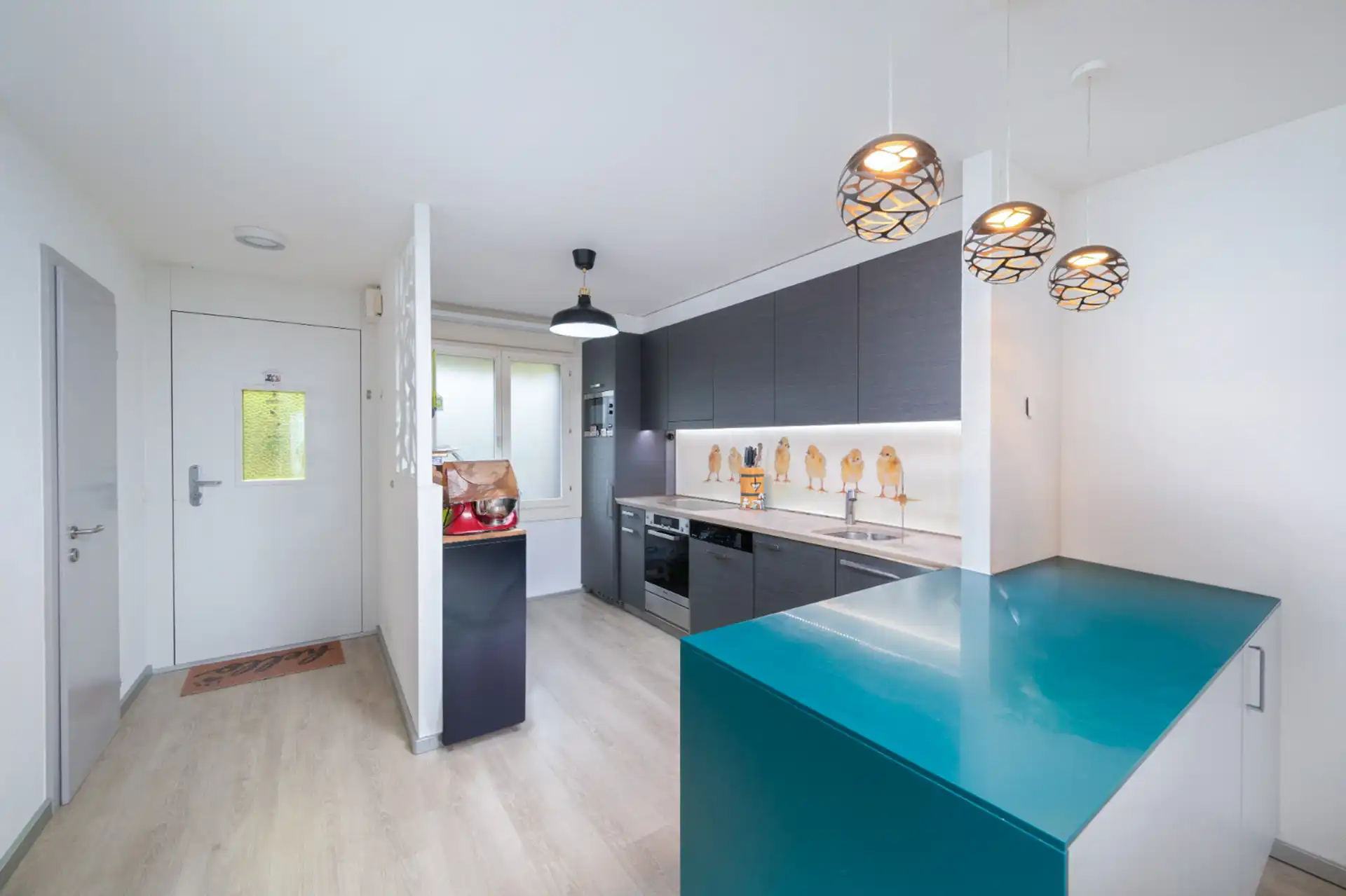 Cuisine moderne ouverte avec ilot central turquoise et électroménagers encastrés