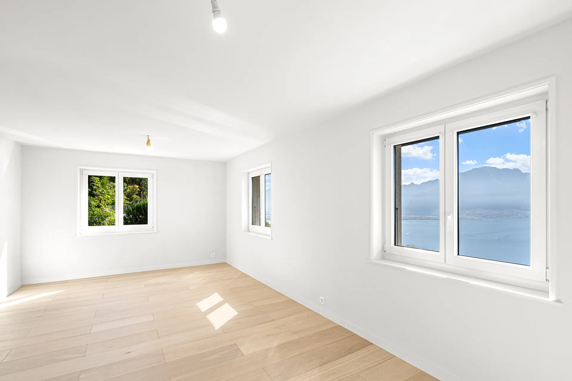 Chambre avec parquet clair et grande fenêtre sur la verdure