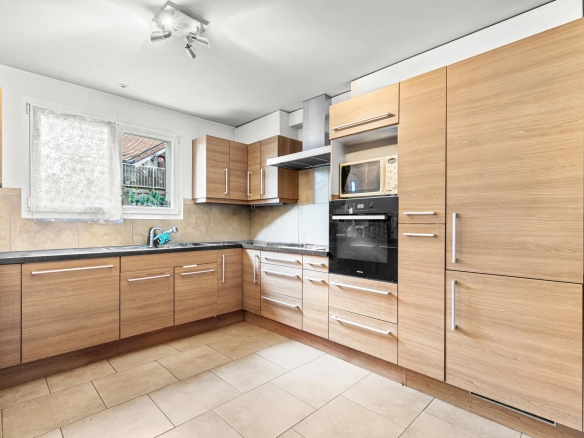 Cuisine moderne en bois clair avec électroménager intégré et plan de travail en pierre.