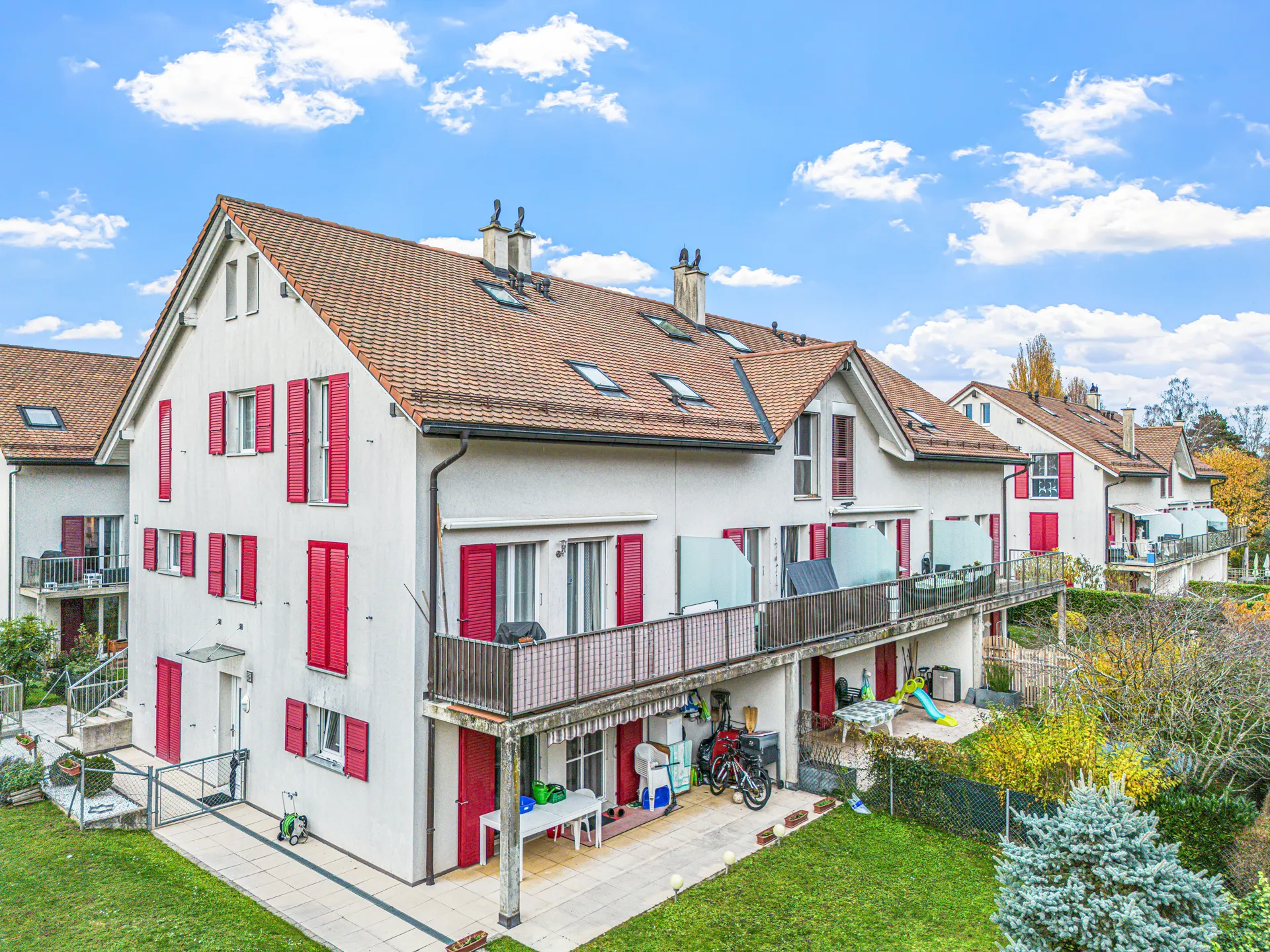 Façade d'un immeuble résidentiel avec balcons et volets rouges, entouré de verdure.
