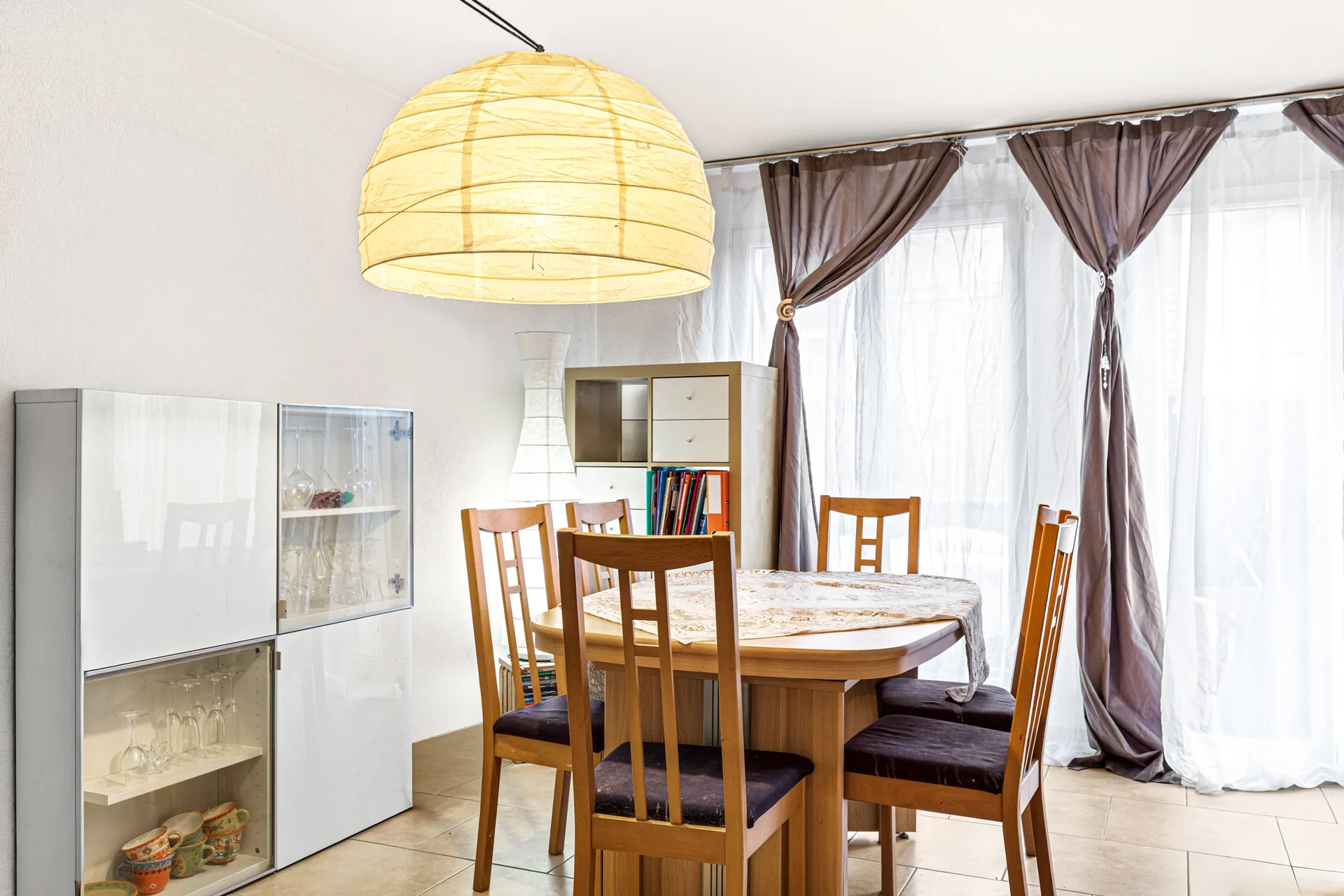 Salle à manger lumineuse avec table en bois et grandes fenêtres donnant sur le balcon.
