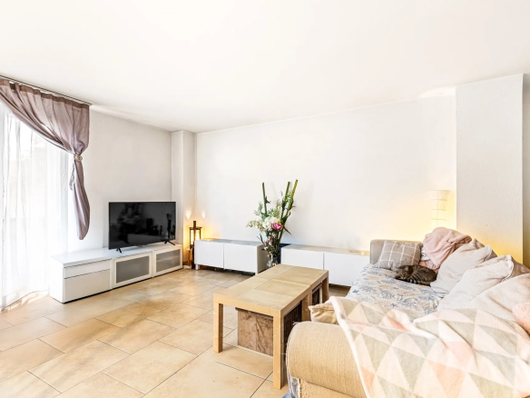 Salon lumineux avec canapé, table basse en bois et grand téléviseur.