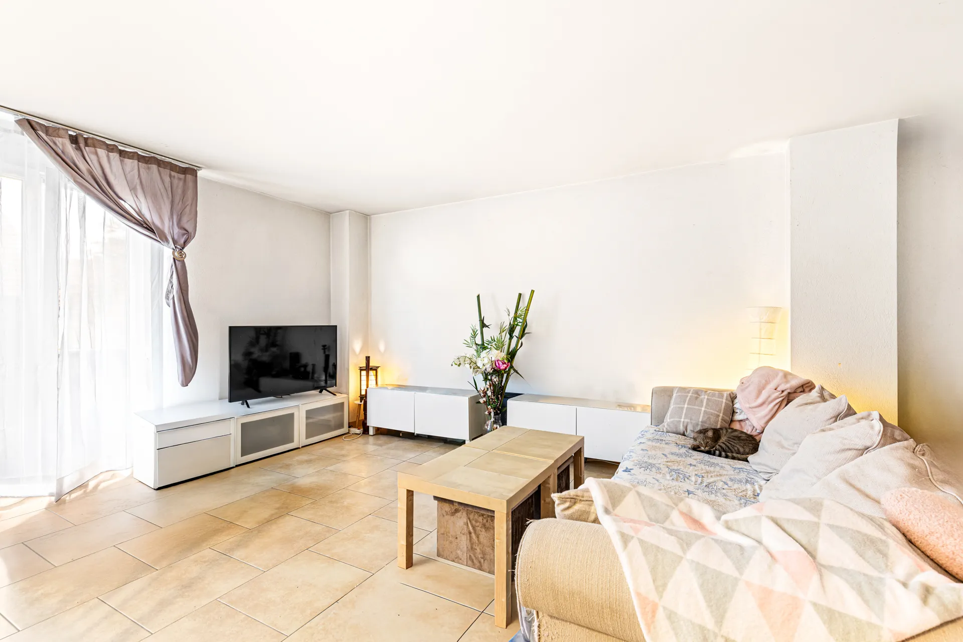 Salon lumineux avec canapé, table basse en bois et grand téléviseur.