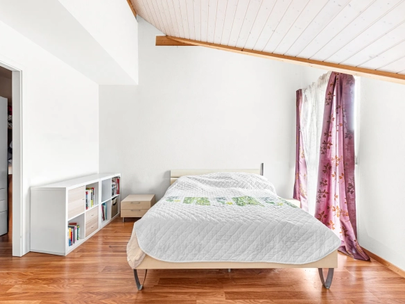 Chambre lumineuse avec lit double, poutre apparente et grande fenêtre.