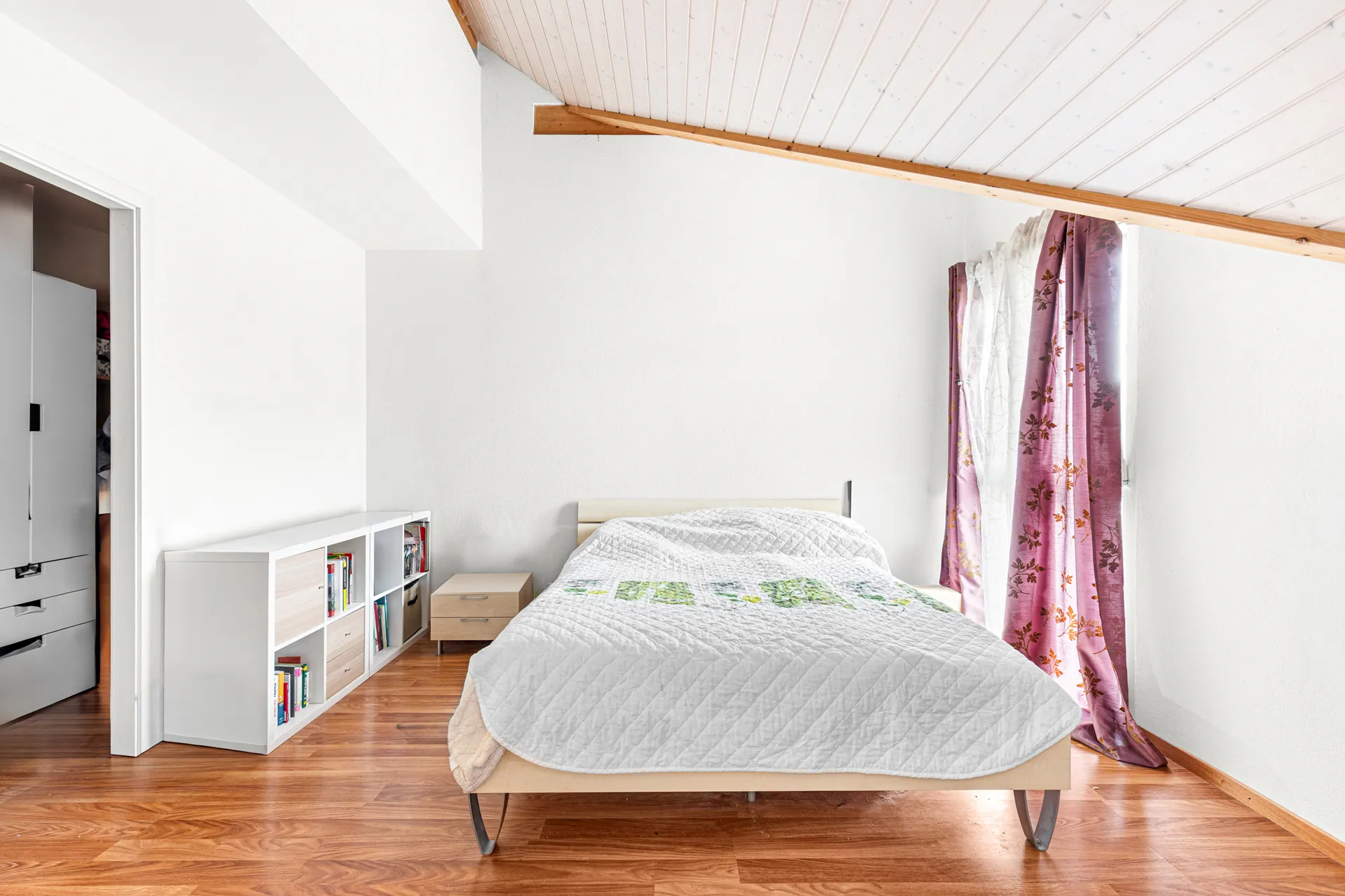 Chambre lumineuse avec lit double, poutre apparente et grande fenêtre.