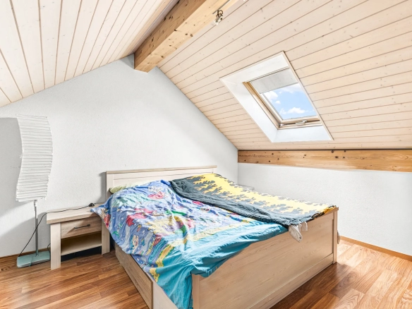 Chambre lumineuse sous les combles avec fenêtre de toit et parquet en bois.