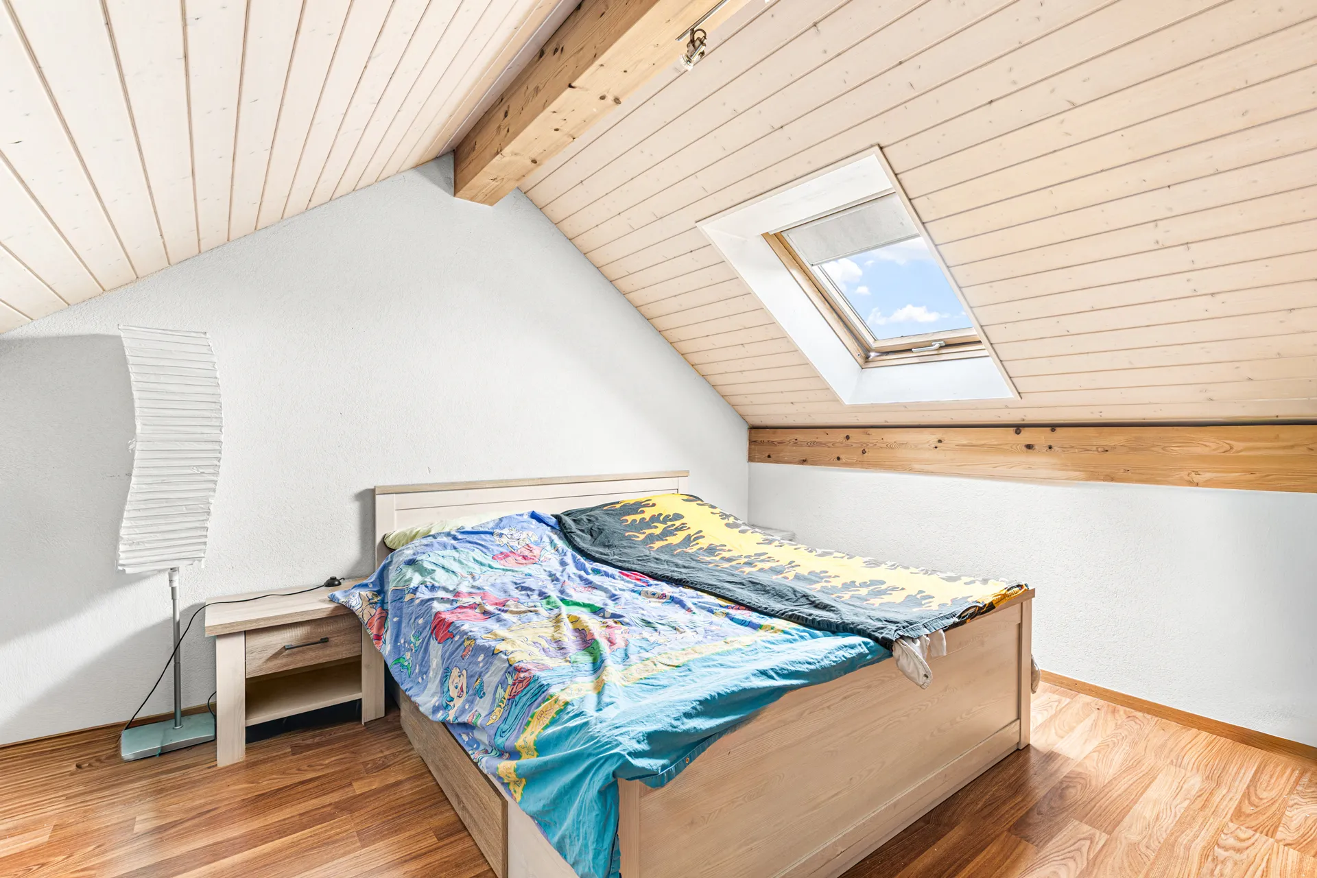 Chambre lumineuse sous les combles avec fenêtre de toit et parquet en bois.