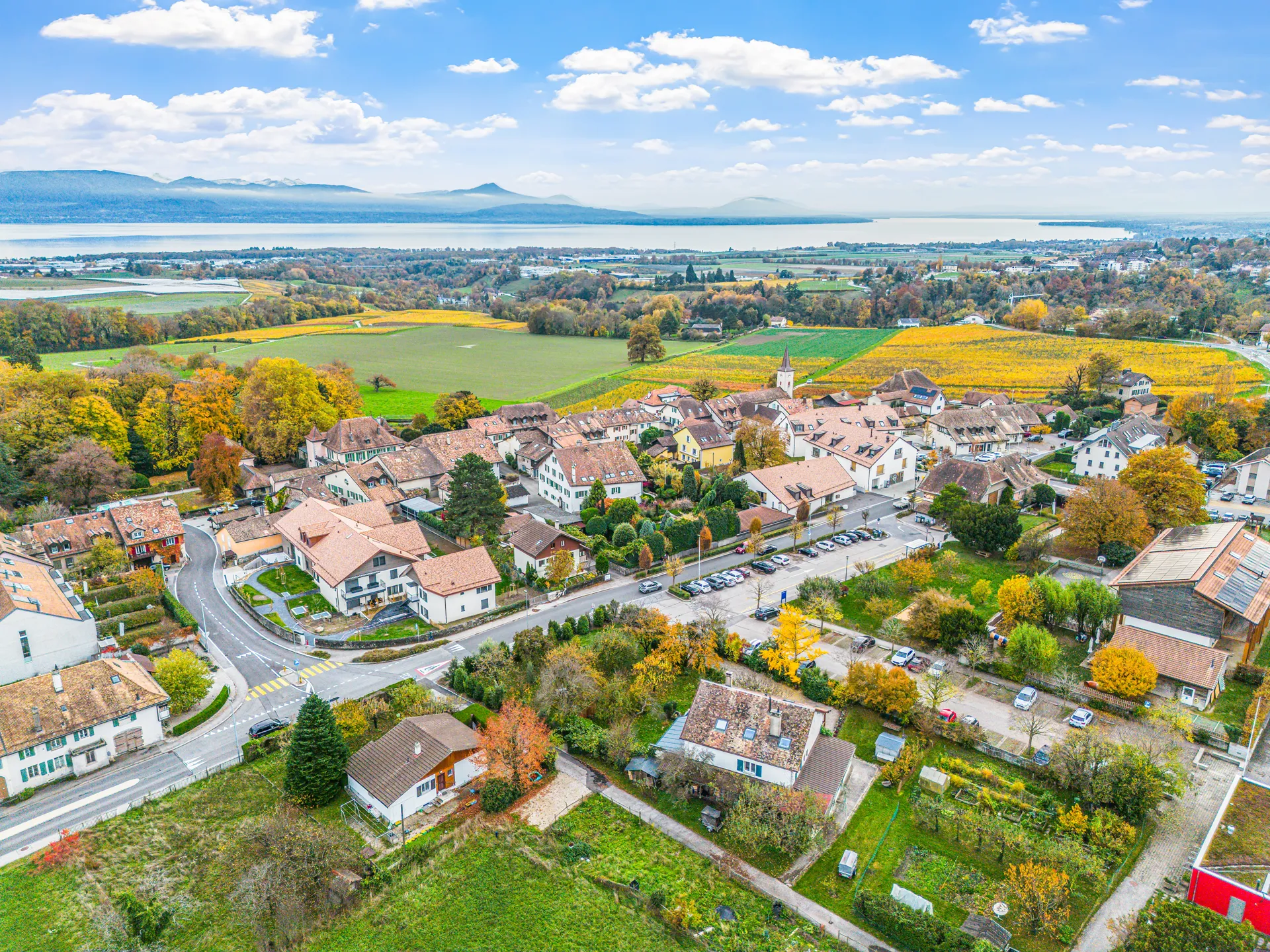 Vue aérienne d’un village entouré de champs et de collines près d’un lac.