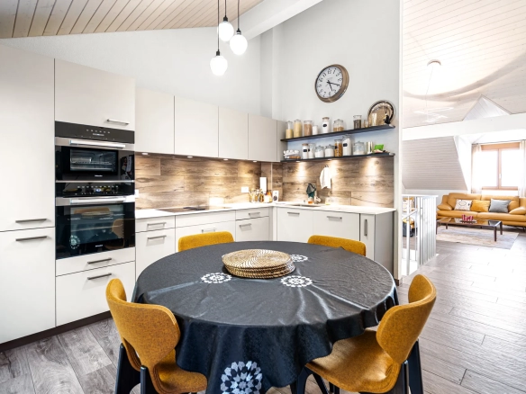 Vue d’ensemble sur la cuisine ouverte et le séjour avec poutres et parquet clair.