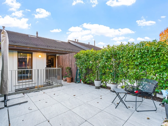 Grande terrasse dallée avec mobilier de jardin et haie verdoyante.