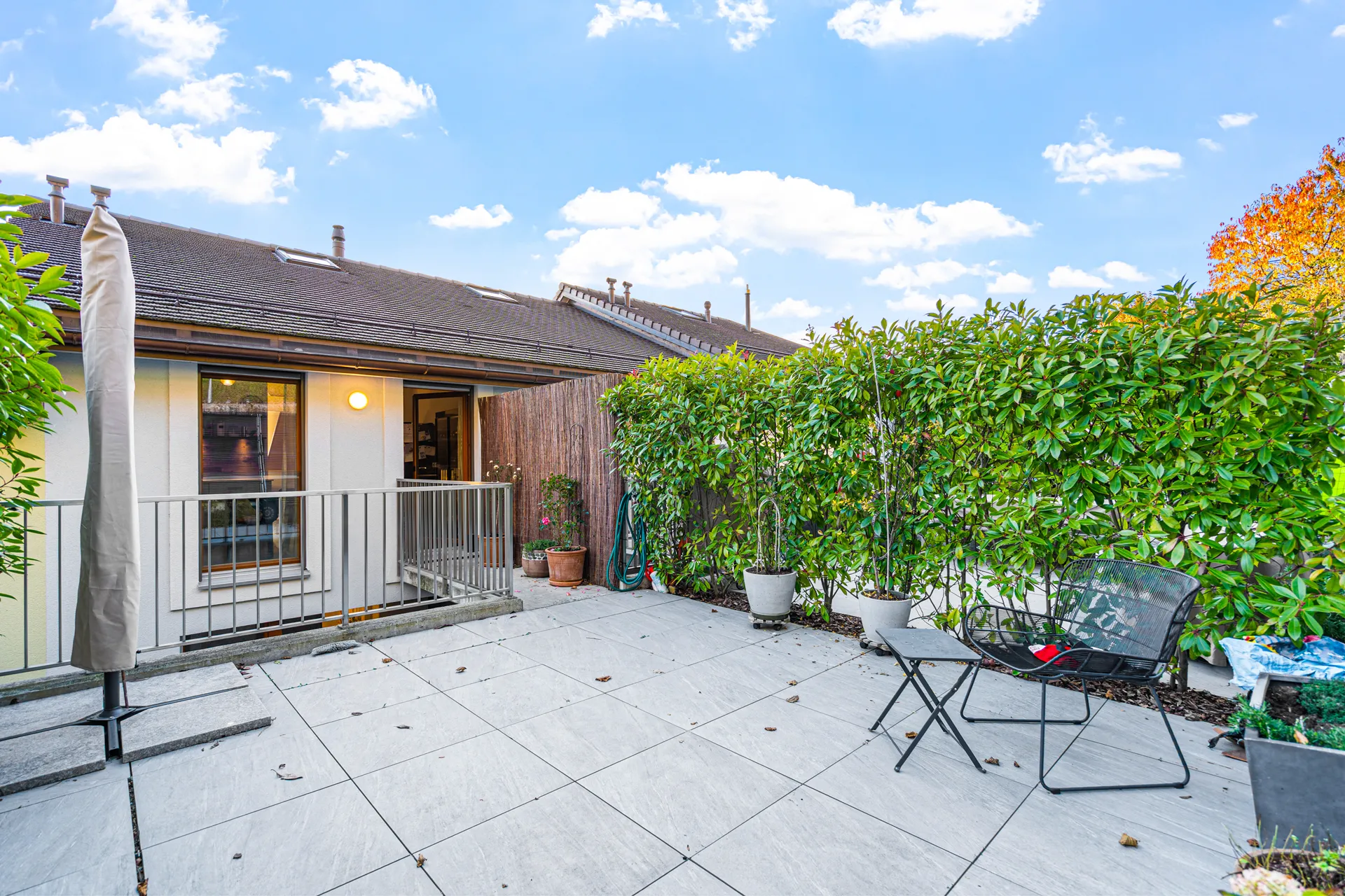 maison-vendre-vuelace-chexbres-immobilier 16 Grande terrasse dallée avec mobilier de jardin et haie verdoyante.